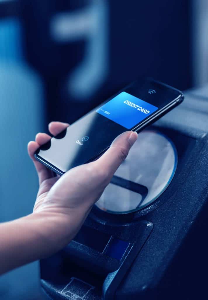 A person holds up their phone to pay for something wirelessly at a kiosk