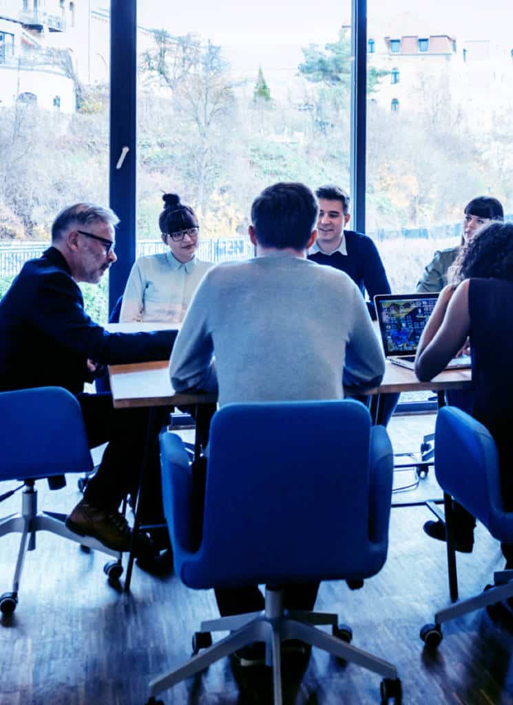 Six business colleagues sitting around a conference table with a wall of windows behind them