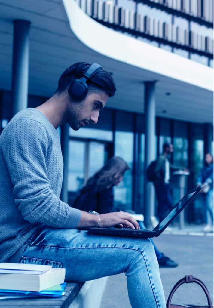 Student wearing headphones sitting on a bench using laptop