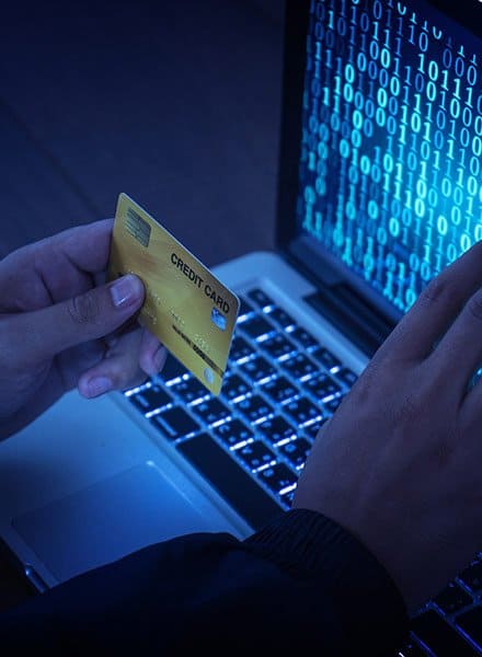 A person with their gold credit card sits in front of their laptop with lines of binary code displaying on the screen.