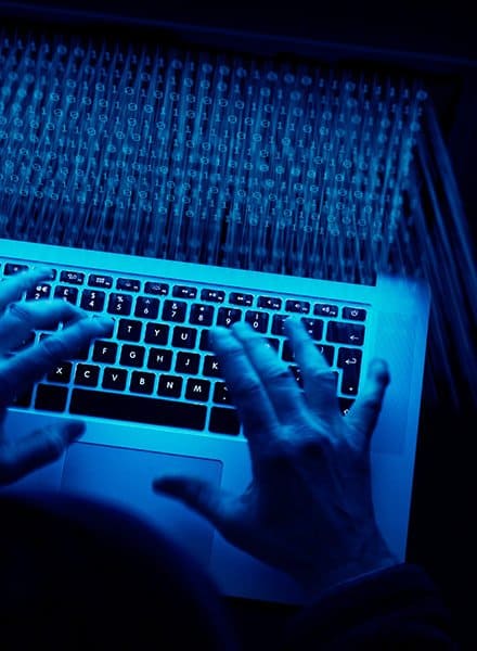 A person is typing on their MacBook Pro, there is a lot of blue light coming off of the screen which is filled with lines of code