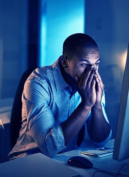 Man looking at a computer screen with hands covering his nose and mouth