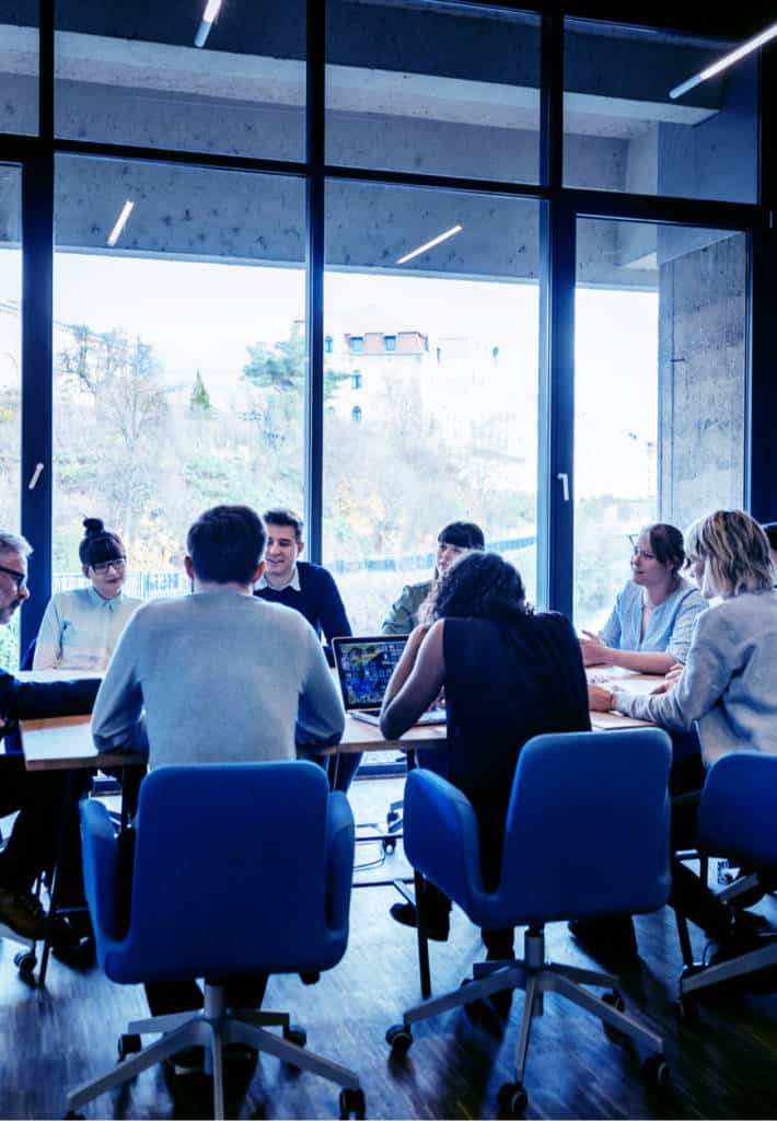Eight business colleagues sitting at a conference table together with a wall of windows behind them