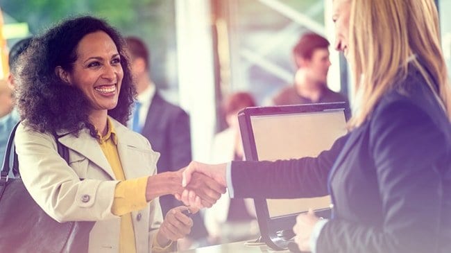 Two women shake hands while others stand in line behind one of them