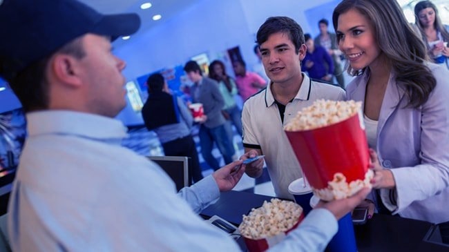 A couple buys popcorn at a busy movie theater