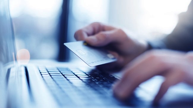 A close up of someone holding their card as they type the information into their laptop.