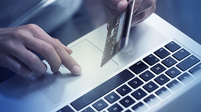Woman has her credit card in one hand and is scrolling on her laptop with the other hand.
