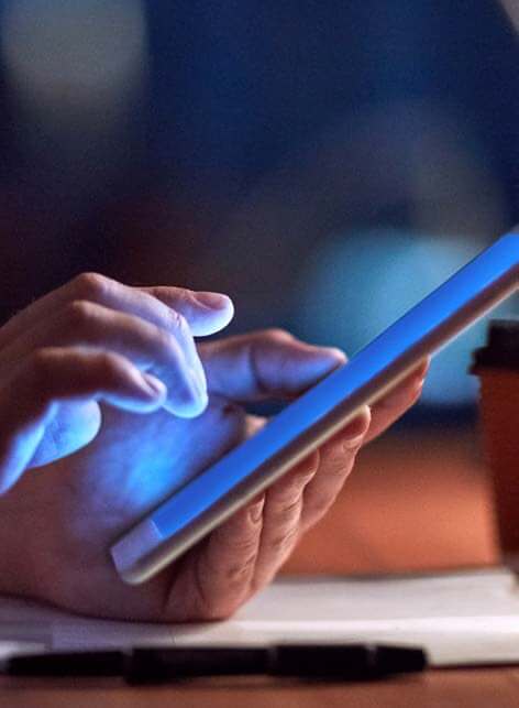Hands typing on a smart phone over a desk in the dark