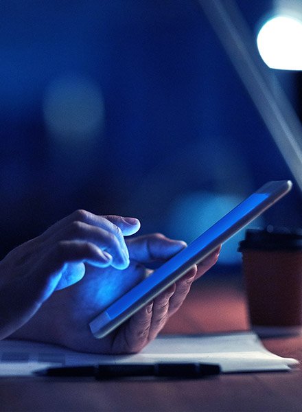 A man is on his tablet browsing while sitting at his desk. 