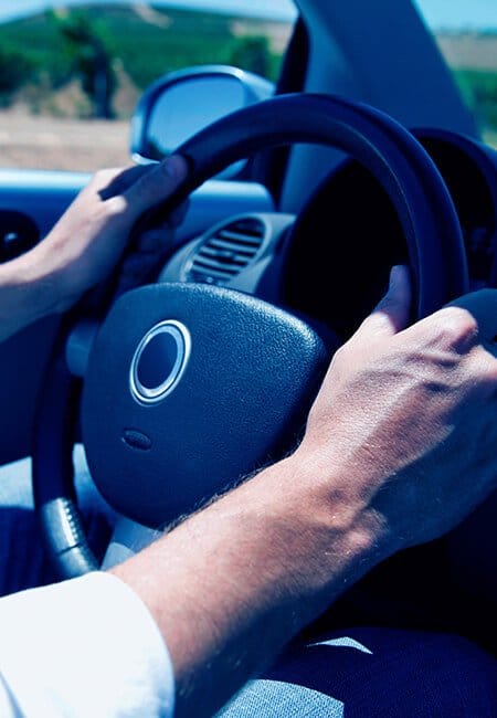 Two hands gripping a steering wheel as they drive.