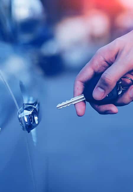 A close up of a hand going to unlock a car door with their car key.