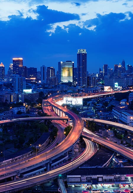 A city skyline at dusk There are light streaks due to a long exposure photo of a highway overpass. 