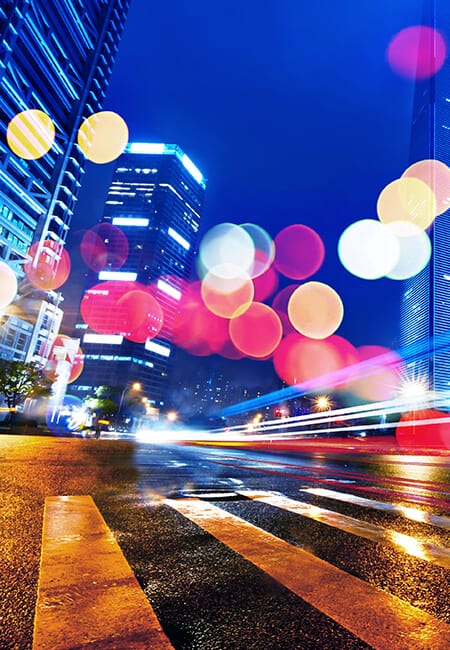 A nighttime shot of a busy intersection with a motion blur of cars passing as well as the bokeh from multiple lights spread across the image.