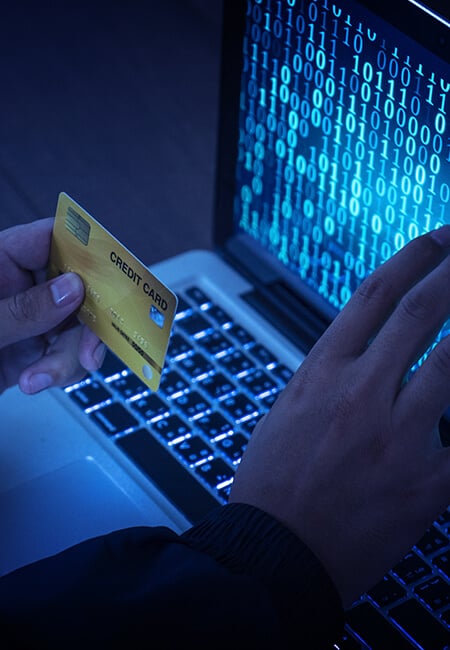 A person with their gold credit card sits in front of their laptop with lines of binary code displaying on the screen.