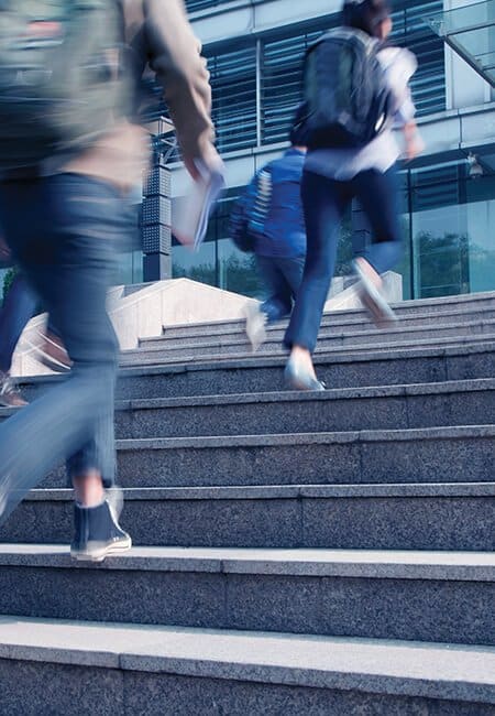 Three people are running up the stairs, they are all wearing backpacks and there is lots of motion blur. 