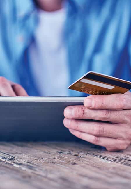 A man is holding a credit card and a tablet, he is entering his information to complete a transaction. 