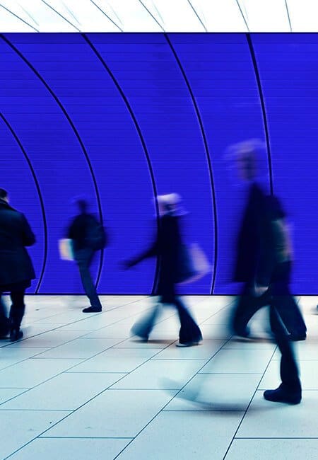 People walking through an underground tunnel with a blue curved wall and clean white tiling, the people moving by are blurred.