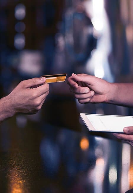 A person hands their credit card to the waiter who is holding an iPad, in order to complete their purchase.