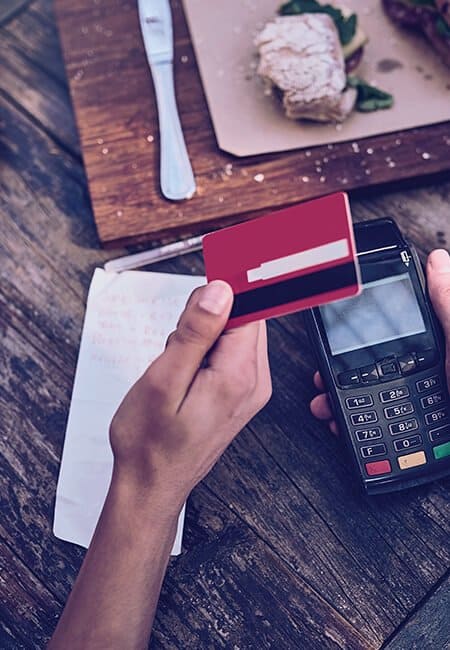 A person is handing a card to their waiter so they can pay for their meal using the card reader. 