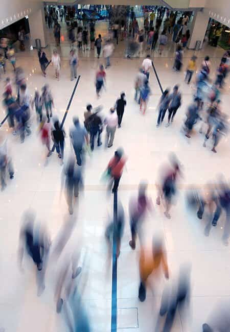 People mingle in a large open indoor space, there are lots of people moving causing a large amount of motion blur. 