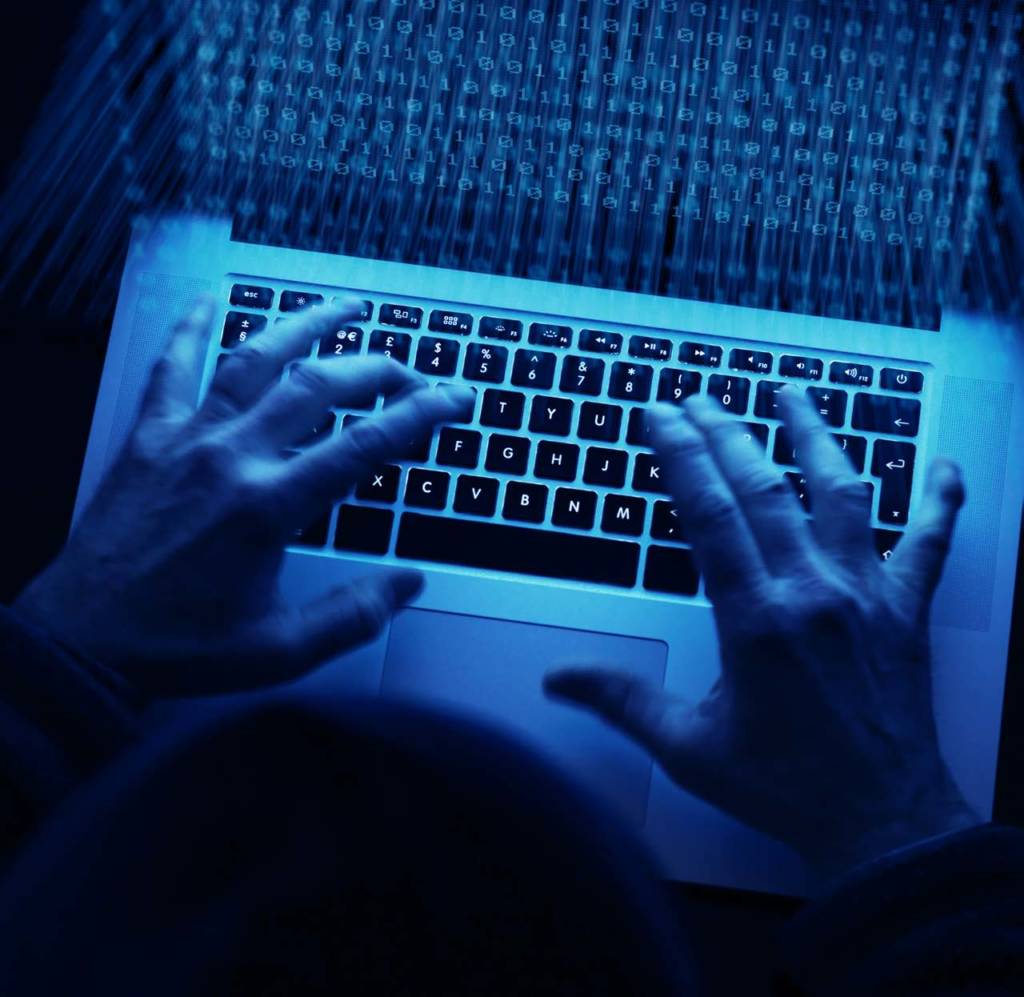 Person typing on laptop in the darkness with only the light of the screen which has code on it