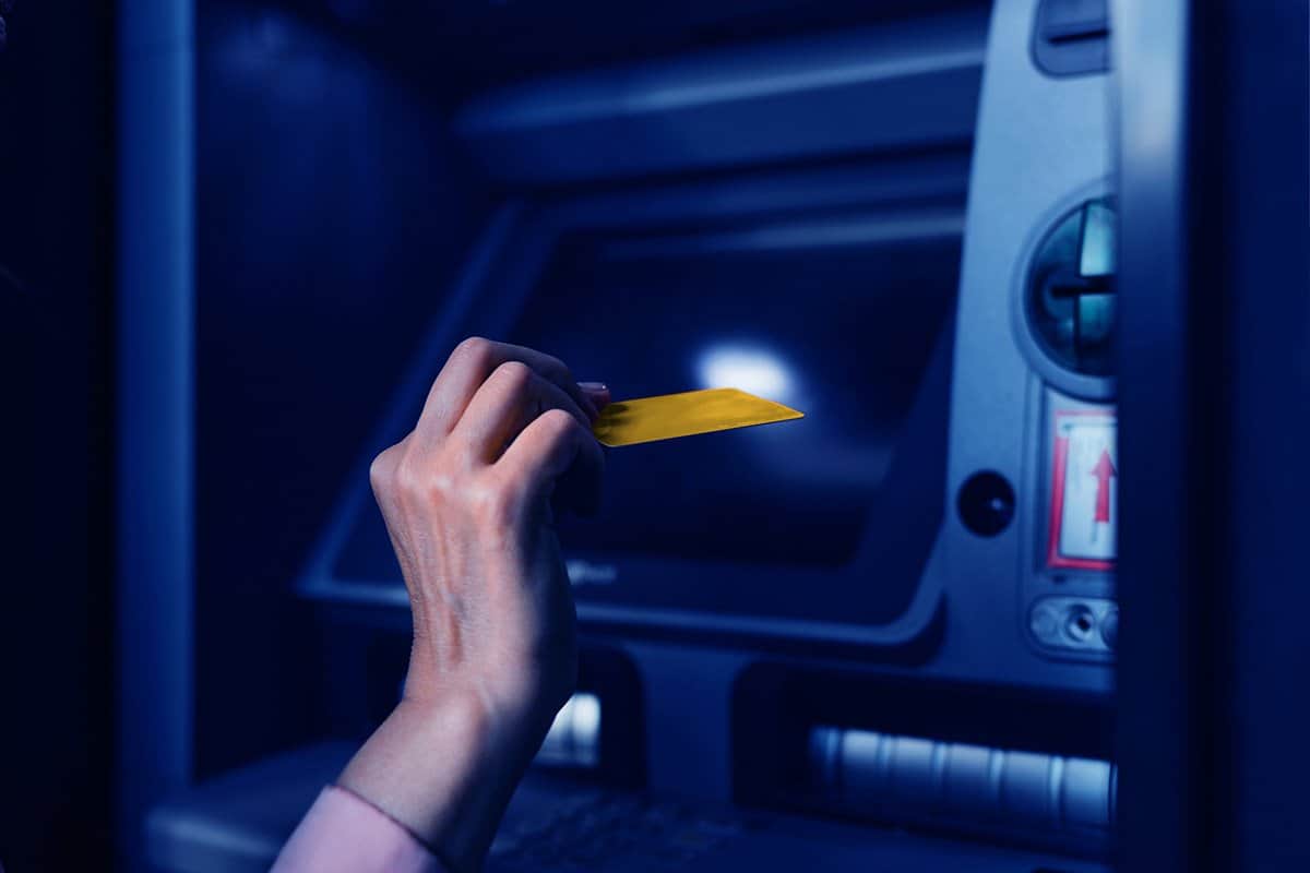 A woman is in front of an ATM machine, she is going to put her gold debit card into the machine to make a deposit or withdrawal from her bank account