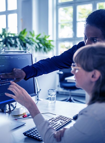 Two business women looking and pointing at code on a desktop computer screen