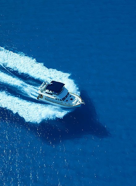 A boat is driving out on a crystal clear blue ocean causing waves to radiate away from the boat as it speeds across