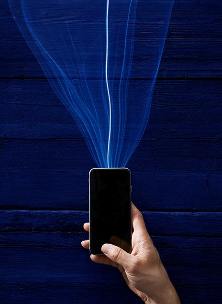 A beam of light representing cellular service strikes the top of an iPhone, as a representation of how cellular data works