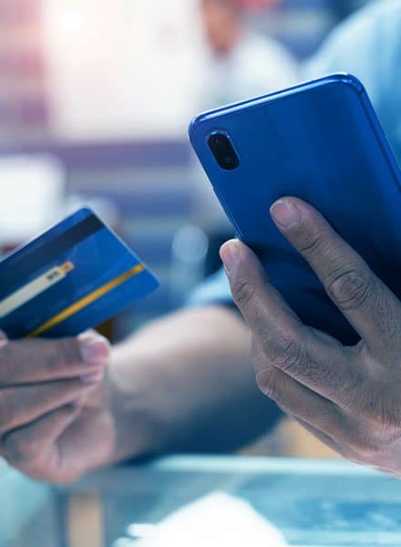 A man is holding his phone in his left hand and his credit card in his right hand. He is entering his information into an online payment service.