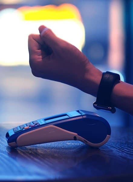 A person uses a smartwatch to pay for a purchase using a tap to pay point of sale system.