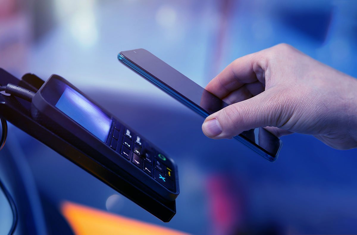 A man holds his phone up to a automatic payment card reader in order to finish his transaction