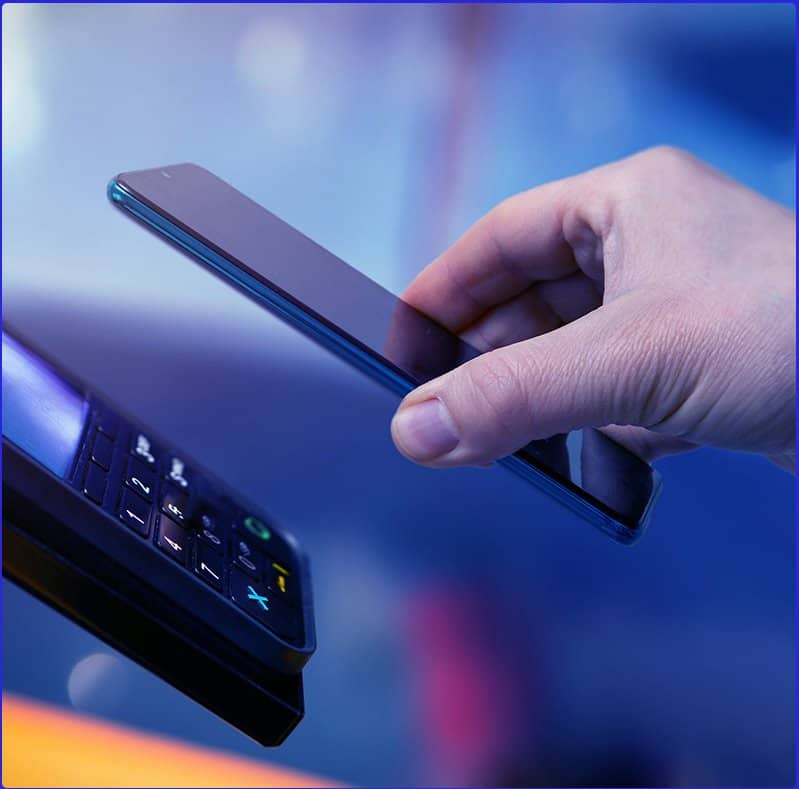 A man holds his phone up to a automatic payment card reader in order to finish his transaction