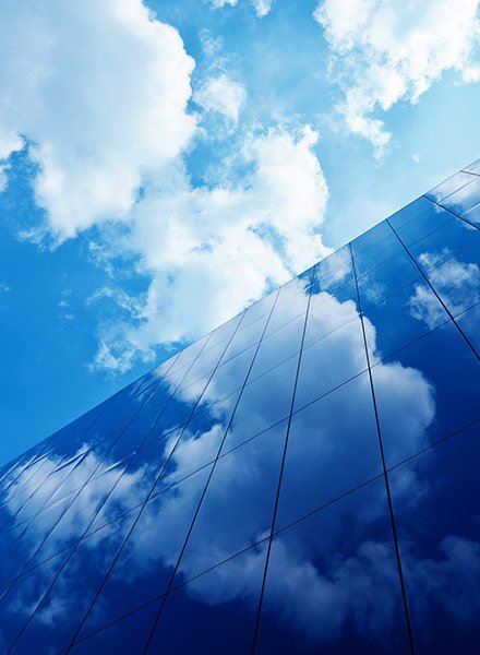 Looking up at the blue cloudy sky with building windows reflecting the clouds