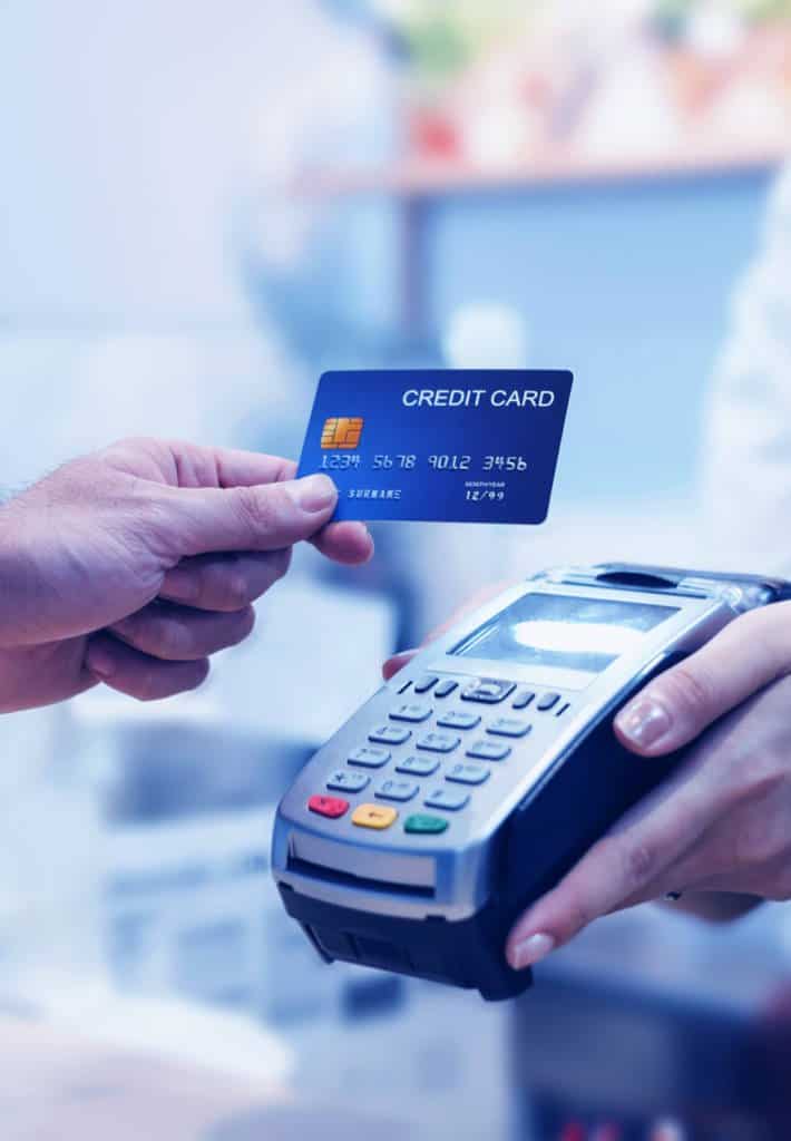 A person uses their credit card to finish up payment at a point of sale system being held by the cashier.