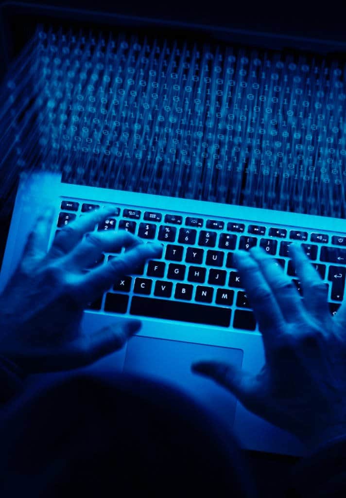 Persons hands typing on a laptop with code motion blurred on the screen in a dark room