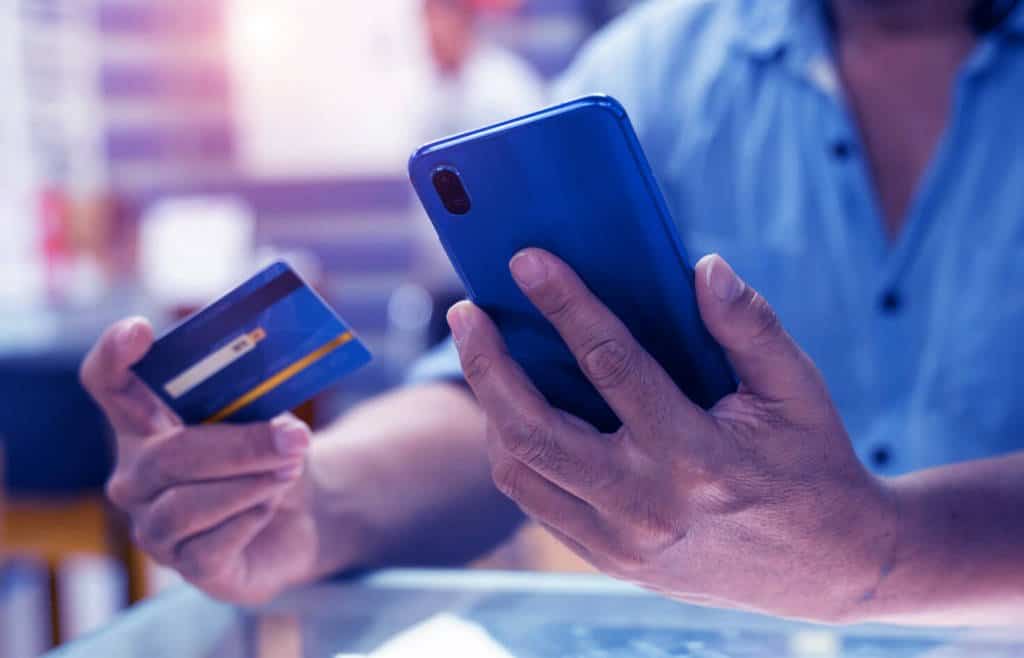 A man is holding his credit card while holding his phone in the other hand