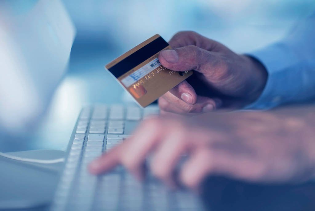Person typing on a keyboard with their credit card in their other hand