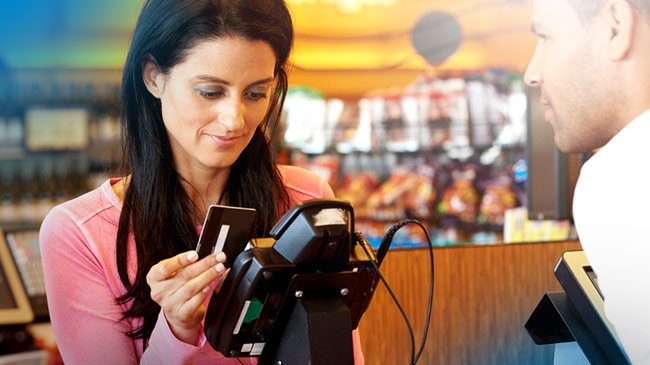 A woman is sliding her credit card through the point of sale system while the cashier observes