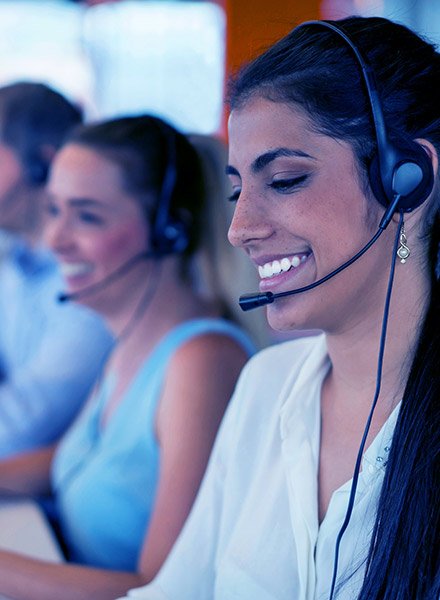 A woman is smiling while working at a call center, her coworkers are behind her. 