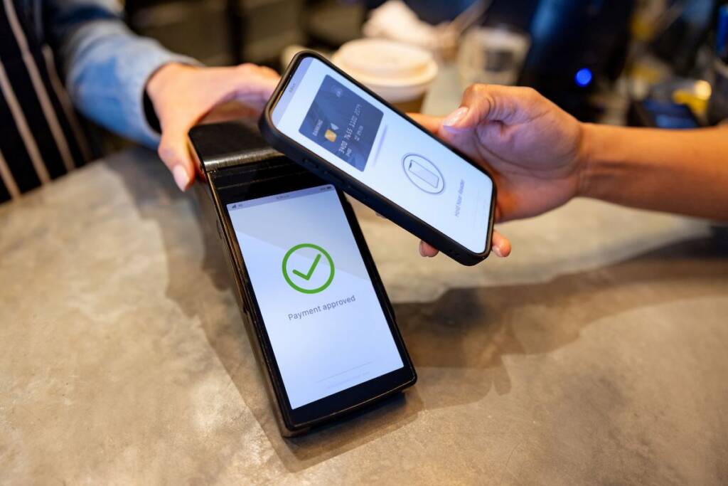 Mobile payment transaction with contactless card and smartphone at a cafe.