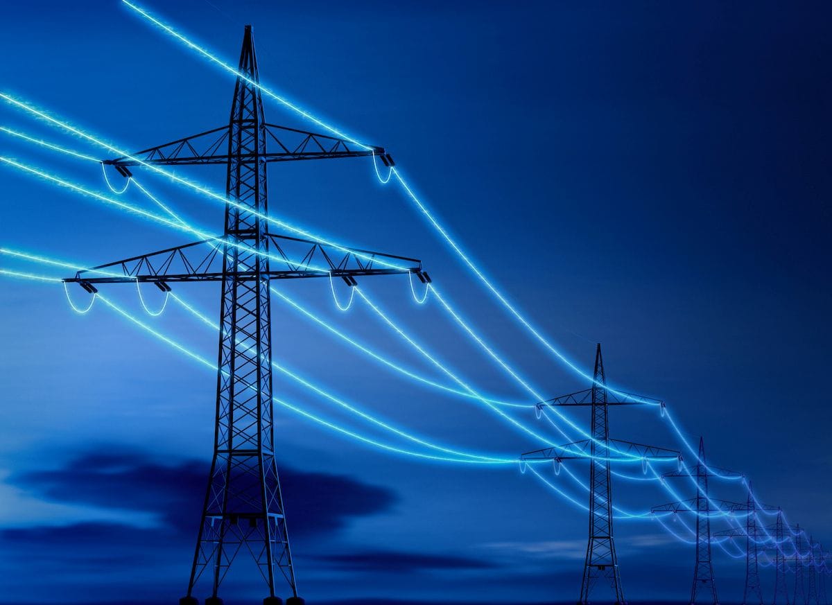 High voltage power lines with illuminated cables against a dark sky.
