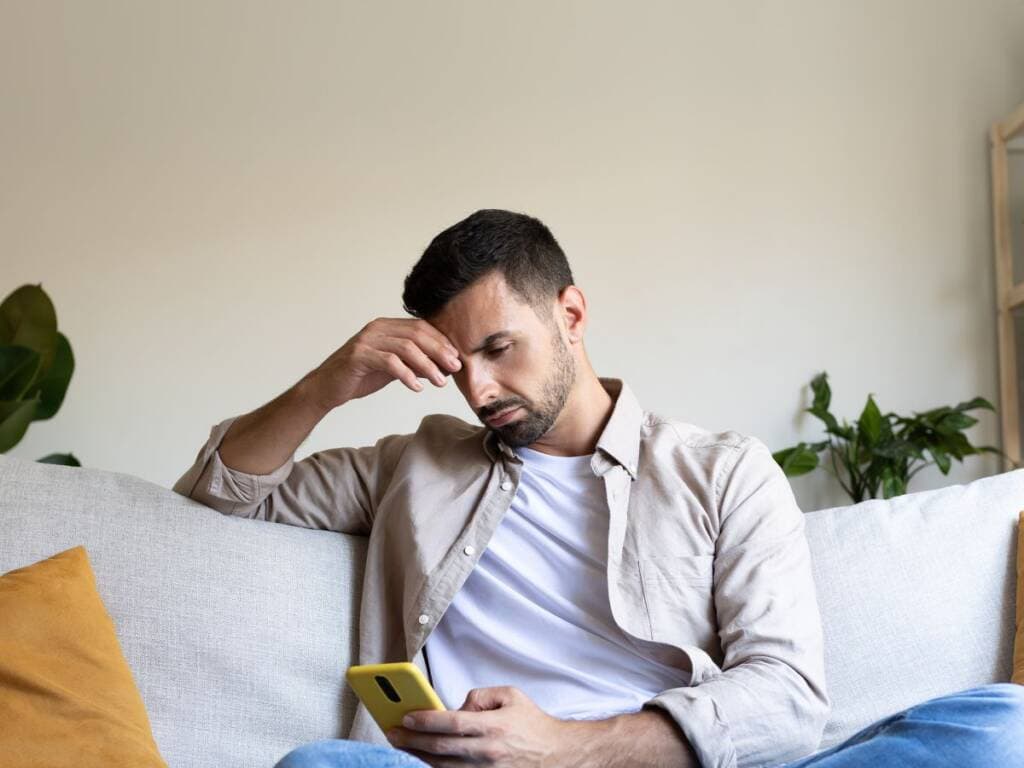 Man looking stressed while using smartphone at home.